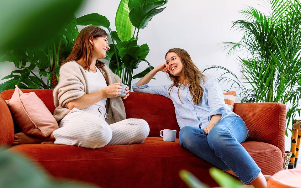 Zwei Frauen sitzen auf einem Sofa umgeben von sehr großen Zimmerpflanzen